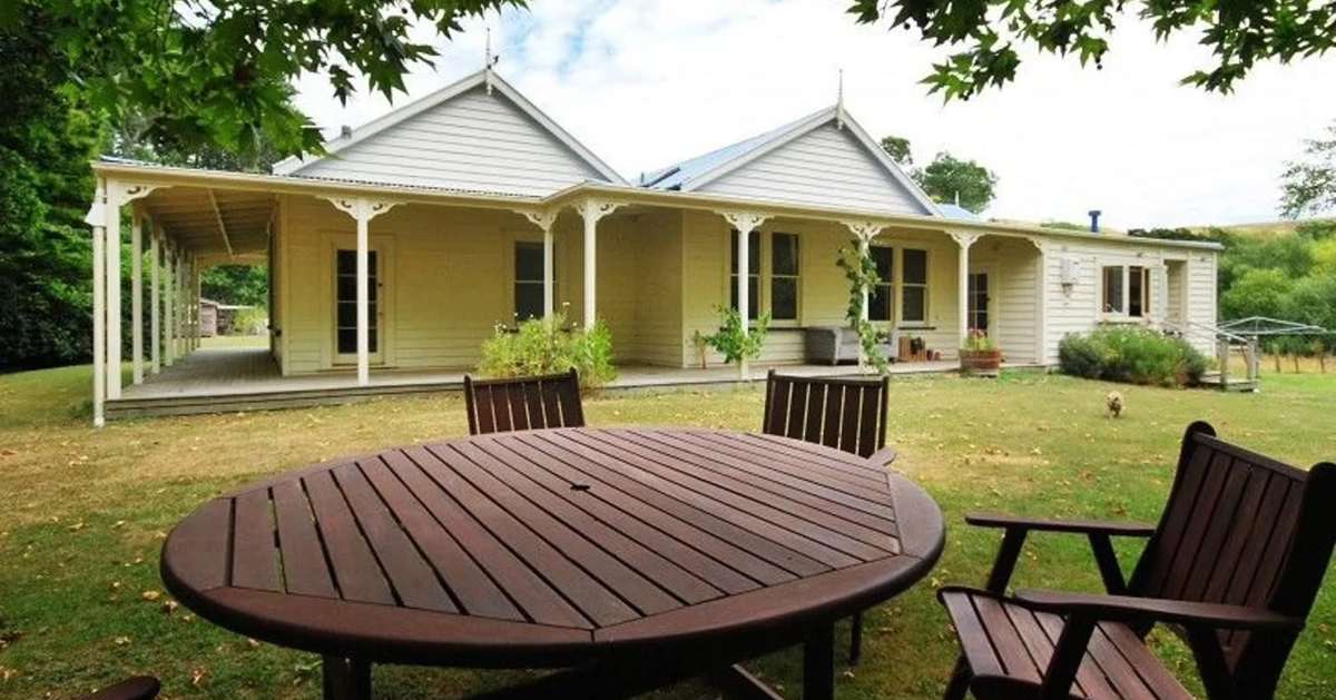 Hillsworth Homestead, a cream weatherboard homestead with a wide veranda and a table on the lawn, near Masterton